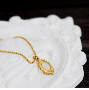 Macro detail of golden oval shell pendant on a bead chain over a white tray