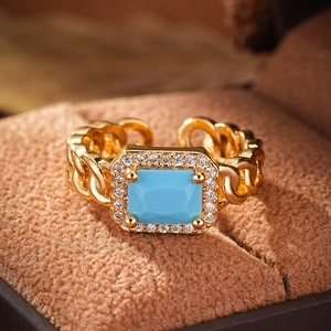 Macro detail of adjustable gold chain ring featuring a blue gemstone and white zirconias