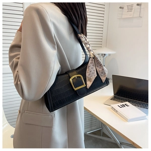 Detail of black crocodile texture baguette bag with golden buckle and silk scarf detail
