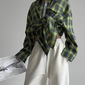 Détail d'une chemise à carreaux jaune et vert nouée avec un pantalon de jogging blanc
