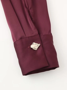Detalle del puño de camisa de satén burdeos con un botón decorativo de metal plateado