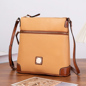 Detail of lychee textured leather crossbody bag with golden metal plate and zippers