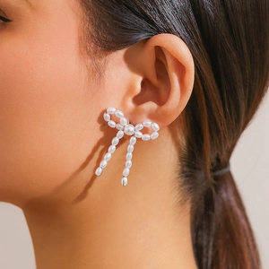 Close-up of elegant pearl bow earrings featuring drop chains on a model profile
