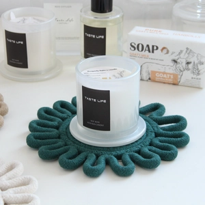 Macro detail of dark green hand-woven cotton coaster in petal shape with candle