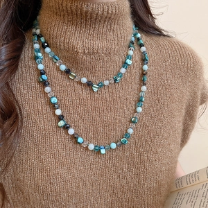 Detail of layered bohemian necklace with turquoise beads and shell accents on brown sweater
