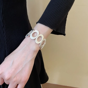Close-up of matte silver hollow oval link bracelet styled with a black knit sweater