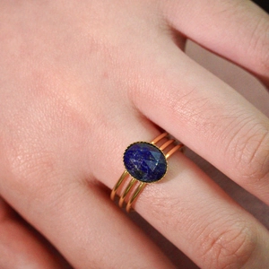 Macro detail of gold multi-band ring featuring an oval blue lapis lazuli stone on hand