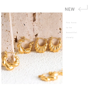 Detailed close-up of golden twisted hoop earrings on a textured stone surface
