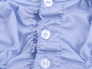 Close-up of light blue shirred poplin fabric featuring three white circular buttons