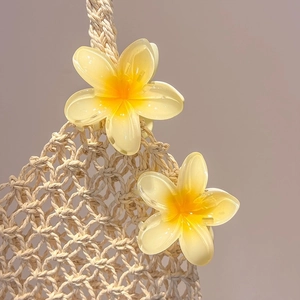 Close-up of yellow gradient frangipani flower hair clips on a woven mesh bag detail
