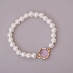 Macro view of white faux pearl bracelet featuring a pink gemstone pendant with gold trim