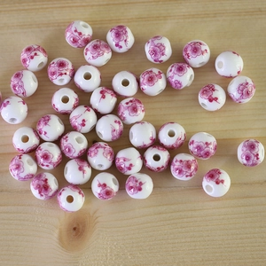 Detail view of round white ceramic beads with pink flower patterns for DIY jewelry making