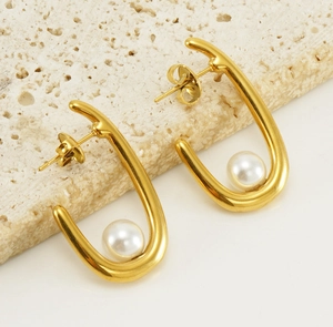 Gros plan de boucles d'oreilles en U dorées 18K avec perles sur support en pierre