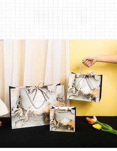 Three sizes of marble patterned gift bags with satin bows and woven handles shown together