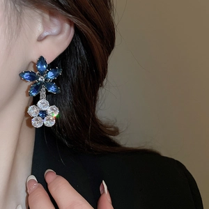 Detail of double-layer flower earrings with blue and white zircons on a female model