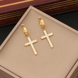 Golden cross drop earrings with inlaid gemstones on a jewelry display cushion