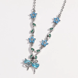 Detail einer Silberhalskette mit blauen Blumenanhängern und einem Schmetterling-Anhänger