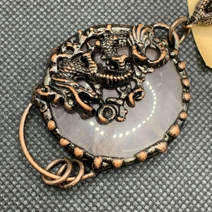 Detailed macro view of a vintage bronze dragon carving over a round pink quartz pendant