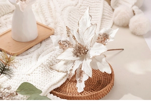 Détail de fleur de Noël en velours blanc avec paillettes dorées sur couverture tricotée