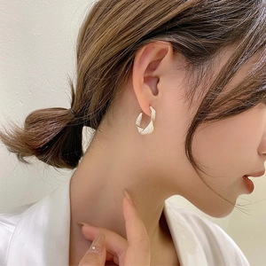 Detail of elegant gold-toned twisted C-shaped earring with white enamel on model