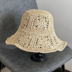 Dettaglio del cappello di paglia beige all'uncinetto con motivi floreali su un supporto
