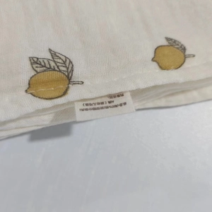 Close-up of 100% cotton muslin baby swaddle with yellow lemon print and safety label