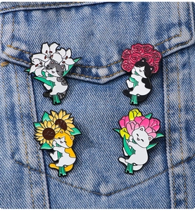 Set of four cute enamel cat pins holding colorful flowers on a blue denim jacket