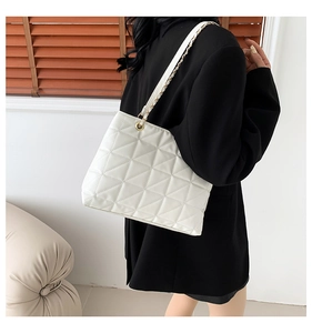 Detail of white quilted shoulder bag with golden chain strap and leather texture