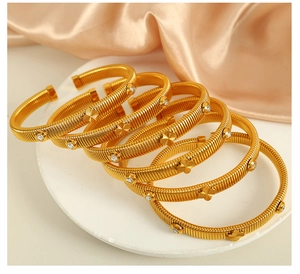 Detail of gold snake-bone bracelets with four-leaf clover motif and white crystals