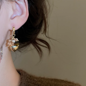 Close-up of golden heart pendant earrings with tiger eye stone and beads on model