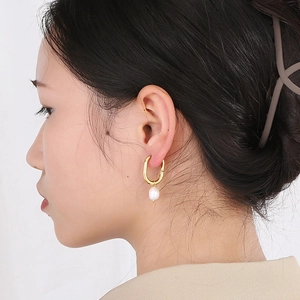 Detailed close-up of a gold U-shaped earring with a white pearl on a model's ear