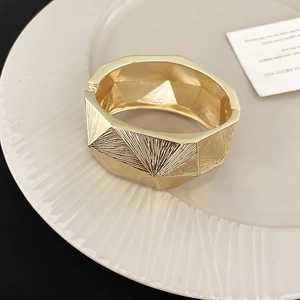 Makrodetail eines goldenen breiten Armreifs mit Polygon-Geometrie und Bürstentextur