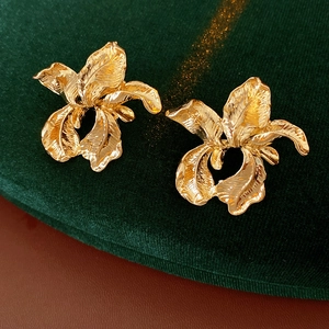 Detailed close-up of golden irregular petal earrings on luxury dark green velvet fabric