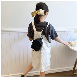 Close-up of a black nylon mini crossbody chest bag worn with a beige satin bow accessory