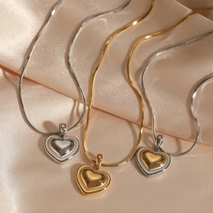 Polished stainless steel heart pendant necklaces in gold and silver on silk background