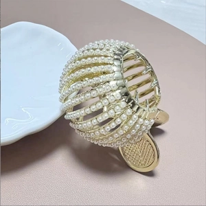 Detailed close-up of golden metal hair claw clip with elegant inlaid white pearls