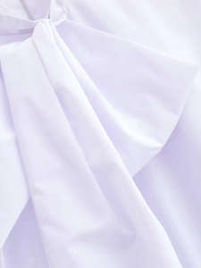 Detail of white cotton blouse neckline featuring a structured bow decoration on smooth fabric