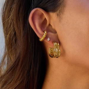Close-up of gold woven ear cuff, teardrop stud and double-hoop earrings set on an ear