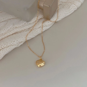 Polished golden heart pendant necklace resting on a beige knitted texture