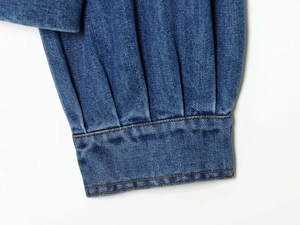 Détail du poignet en denim bleu foncé avec design plissé et coutures jaunes contrastées