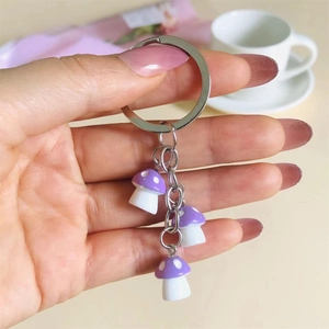 Close-up of hand holding three small purple resin mushroom pendants on a metal keychain