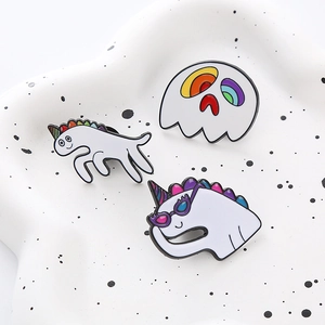 Set of three white unicorn and ghost enamel pins displayed on a ceramic plate