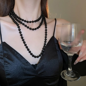 Close-up of elegant multilayered black high-luster faux pearl necklace on silk dress