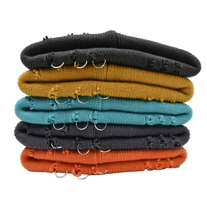 Close-up of stacked colorful knit beanies featuring distressed holes and metal ring details