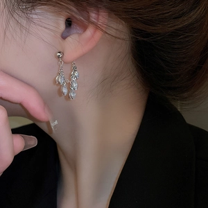 Close-up of silver tassel earrings with zircon leaf charms worn by a female model