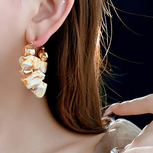 Close-up of model wearing gold beaded earrings with white marble resin geometric shapes