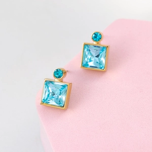 Detail view of geometric square blue crystal earrings with gold base on a pink display