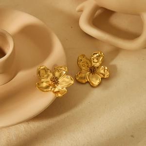 Elegant gold flower stud earrings with pearl centers and wavy petals on beige background