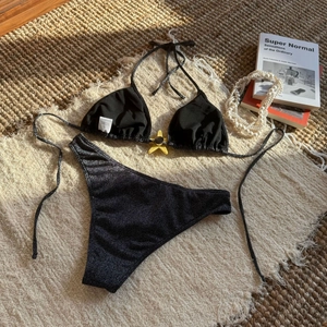 Flat lay of black glitter bikini set with star pendant on a woven vacation mat
