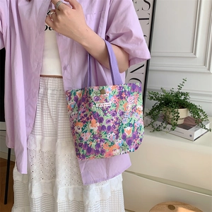 Dettaglio borsa in tela floreale con manici in nastro viola e chiusura a scatto